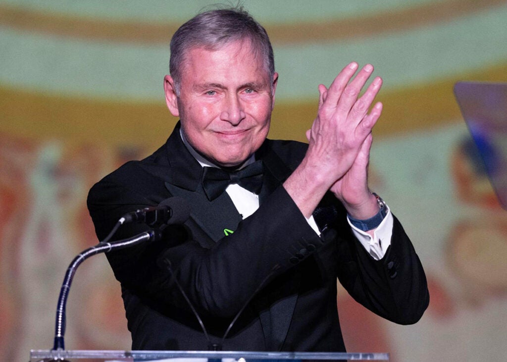 Lou Weiner stands at a podium and  applauds