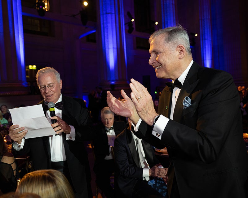 Paul Schweizer reads from a piece of paper while Dr. Weiner applauds