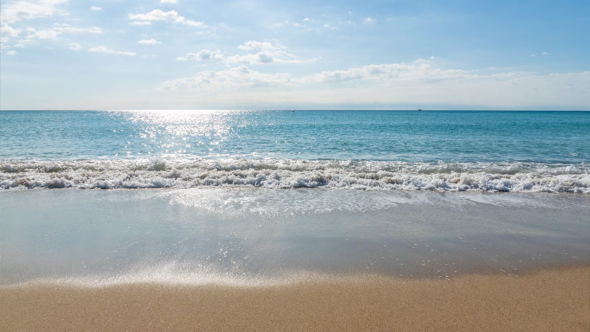 Waves roll onto a beach over which the sun shines