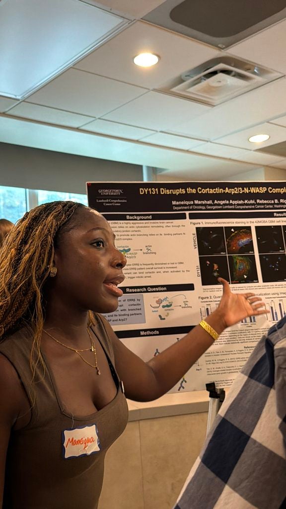 Young woman standing next to her poster and presenting to another person standing by.