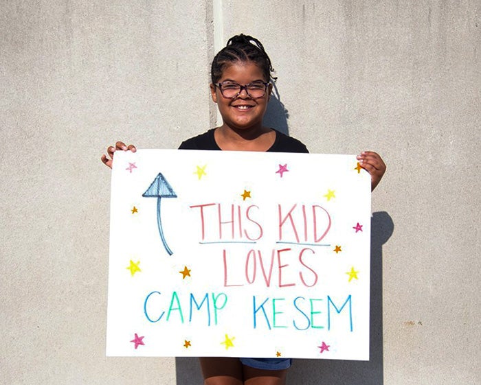 A girl holds a poster with the words This Kid Loves Camp Kesem