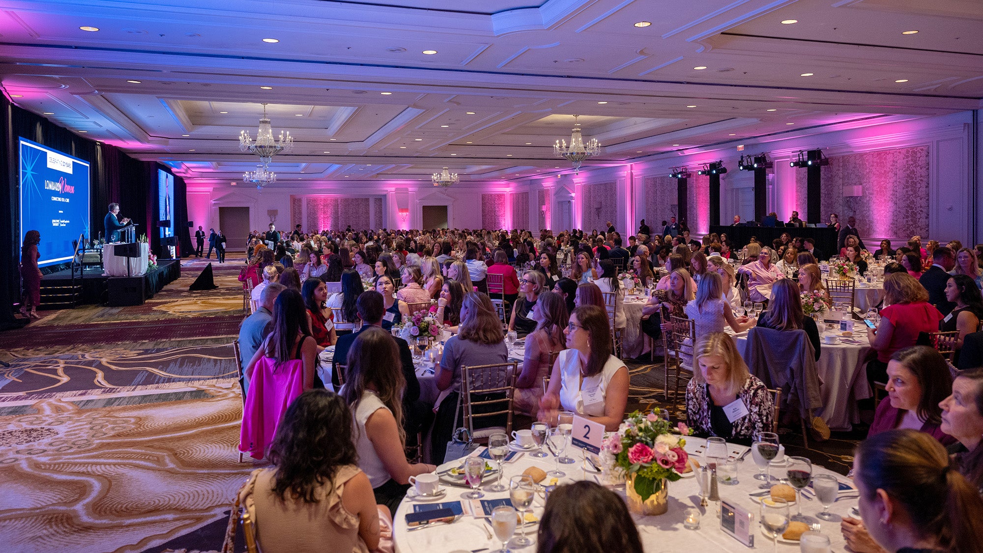 A large ballroom filled with circular tables around which people are seated