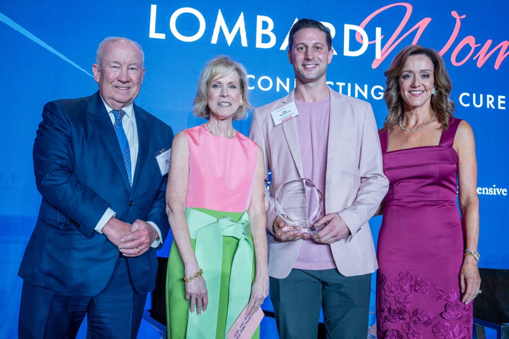 Four individuals stand together, one of them holding an award