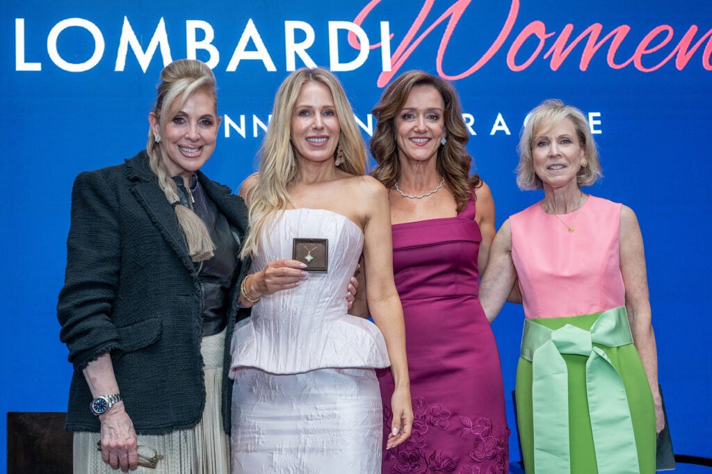 A group of four women stand together, one holding a necklace in a box